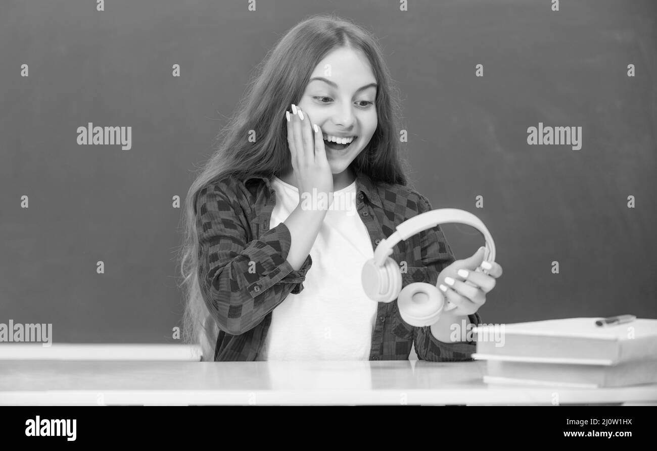sorprendo ragazza teen tenere cuffie moderne in high school a lavagna, scuola Foto Stock