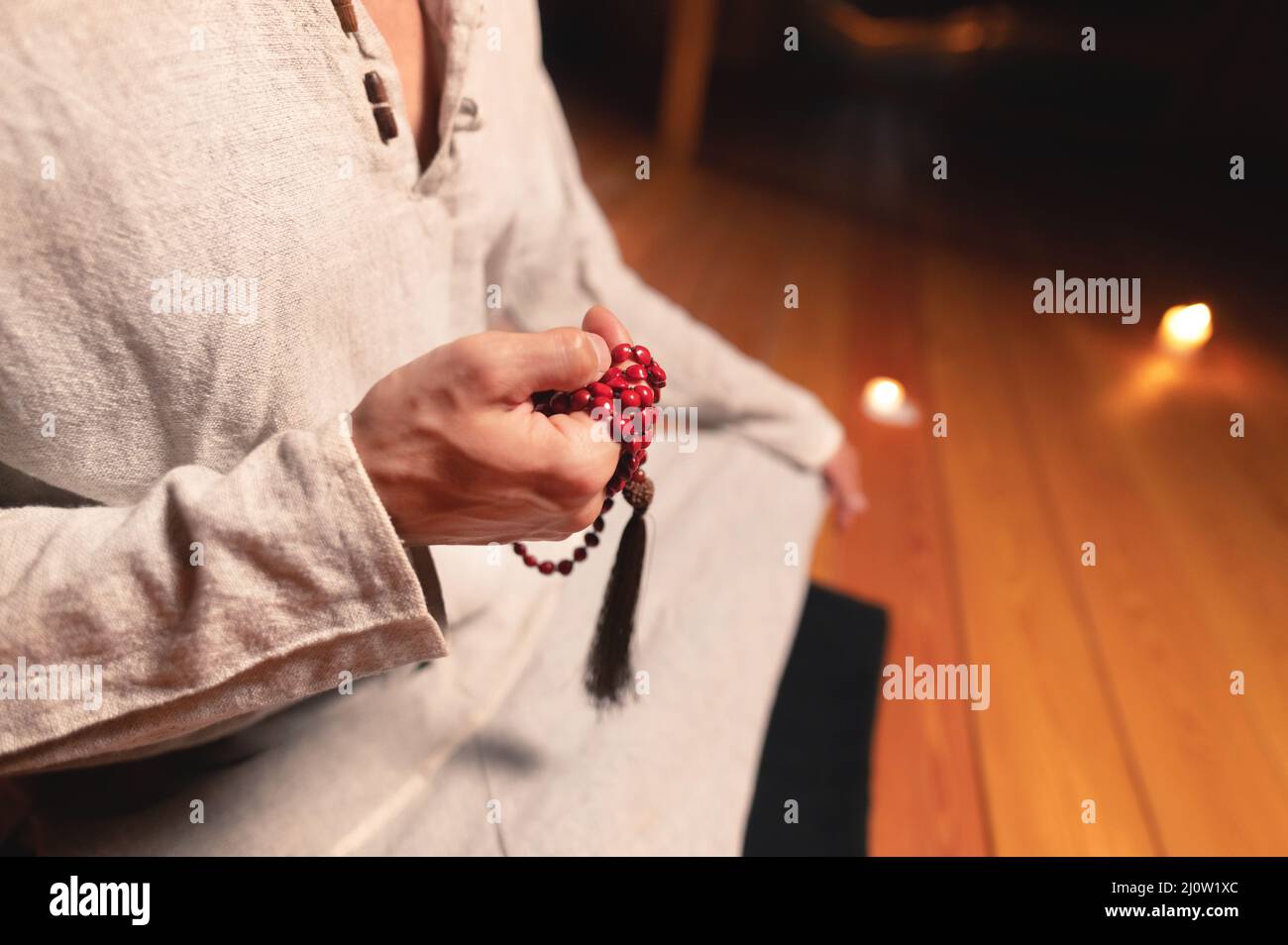 L'uomo in primo piano nei vestiti per la pratica e la meditazione siede in una posa del loto e tiene il rosario rosso per concentrare l'attenzione in un legno Foto Stock