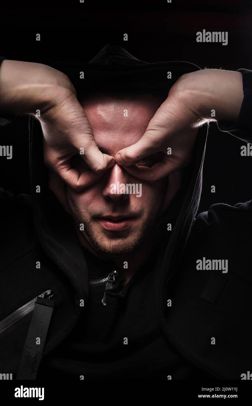 Un ritratto a basso tasto di un uomo in un gesto di mano con cappuccio rende una maschera super eroe. Il concetto di anonimato e privacy Foto Stock