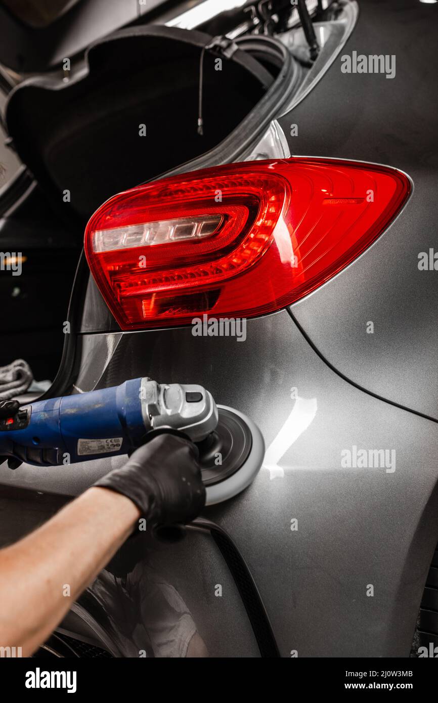 Dettaglio auto e concetto di lucidatura con il lavoratore maschile. Lucidare l'automobile grigia di lusso nel servizio auto. Foto Stock