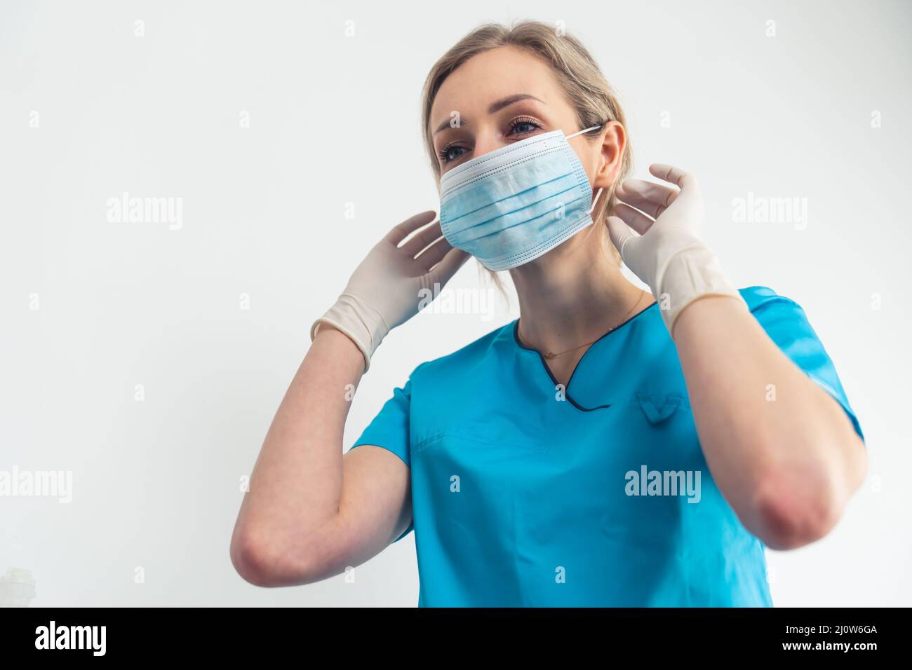 Il giovane caregiver biondo mostra come rimuovere in modo sicuro la maschera chirurgica. Foto di alta qualità Foto Stock