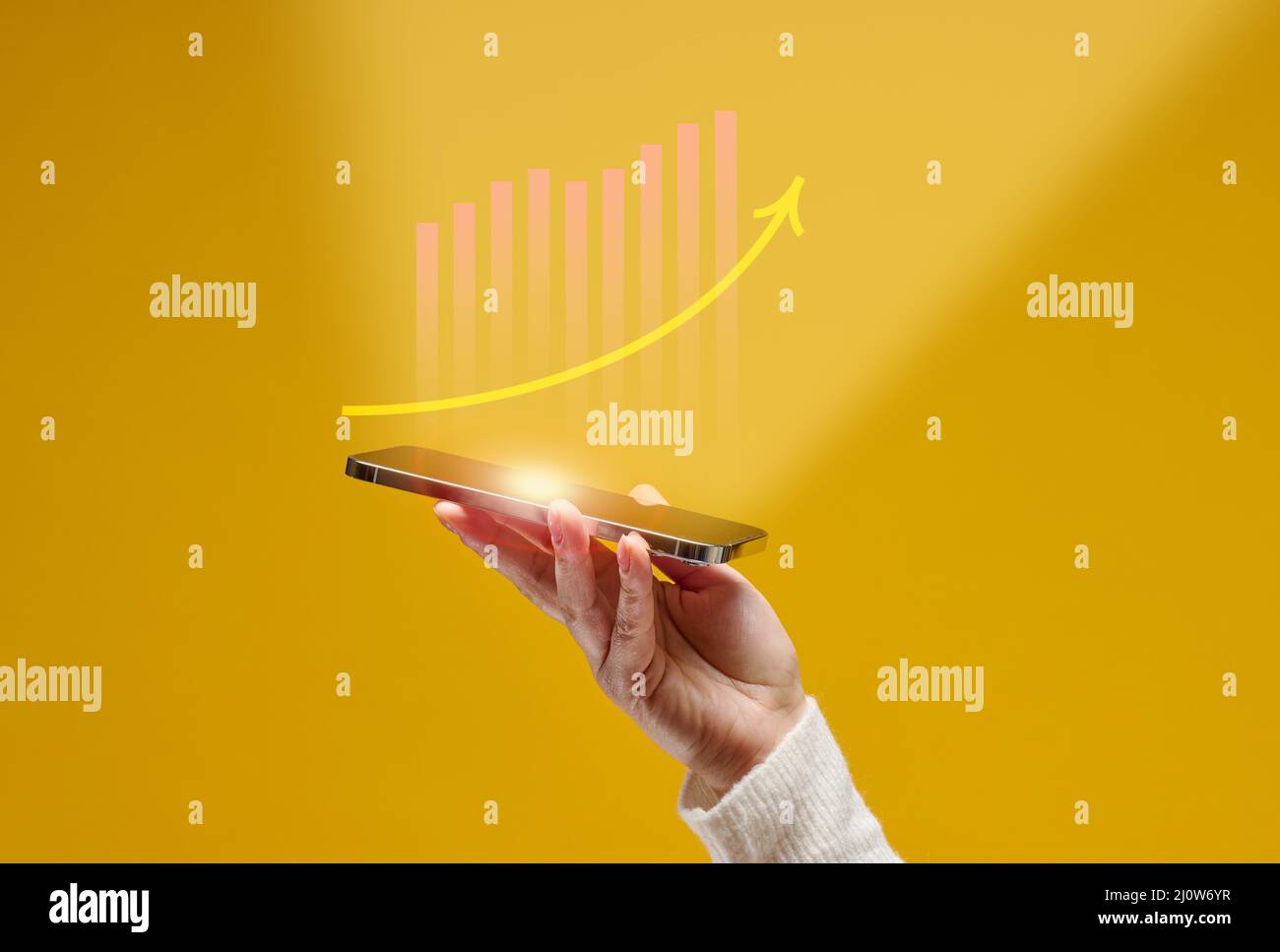 La mano femminile tiene uno smartphone con grafica olografica su sfondo giallo. Crescita delle prestazioni, successo Foto Stock