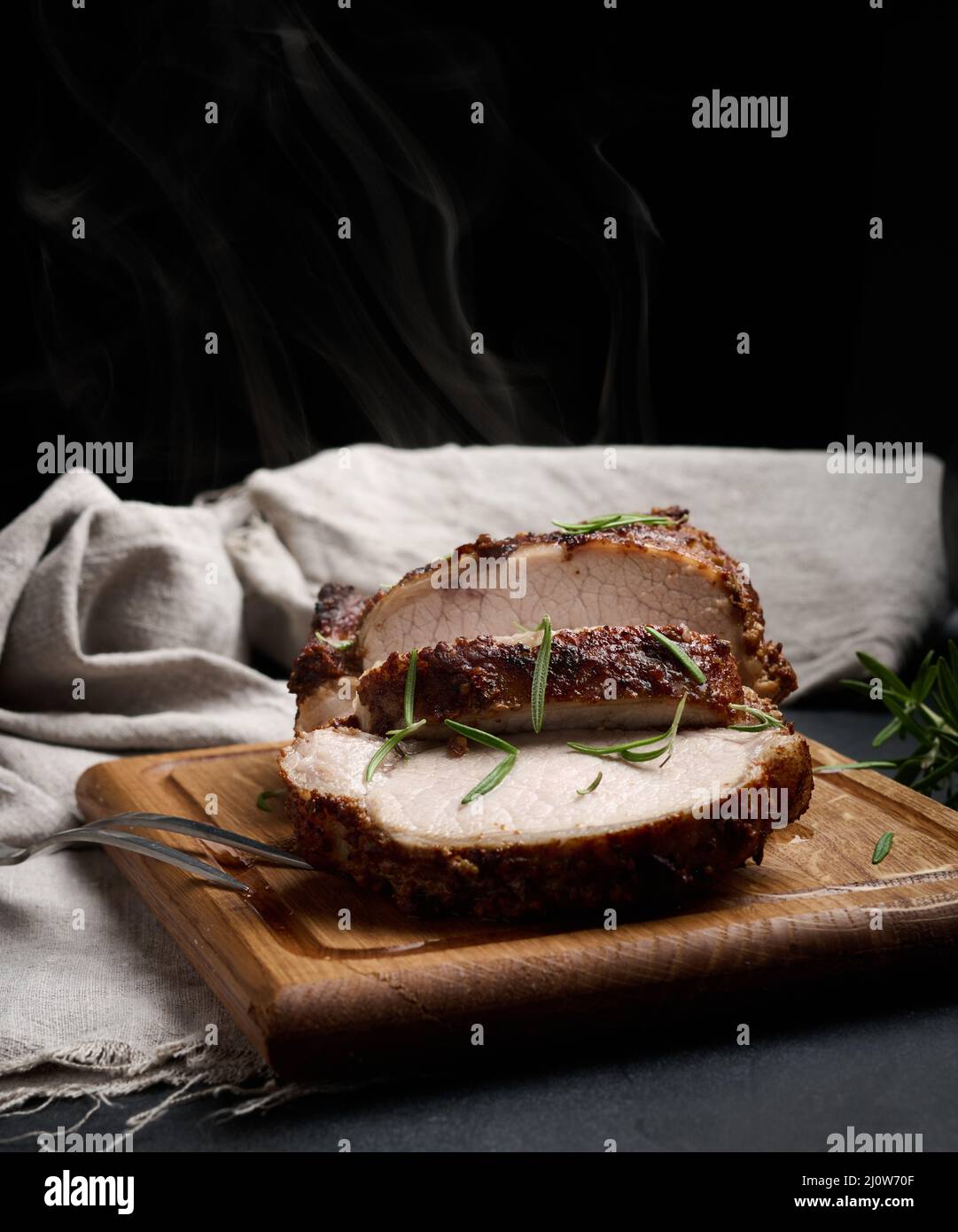 Pezzo di carne di maiale al forno in spezie su un asse di legno, tagliato a pezzi. Occhio di bistecca arrosto rotonda Foto Stock