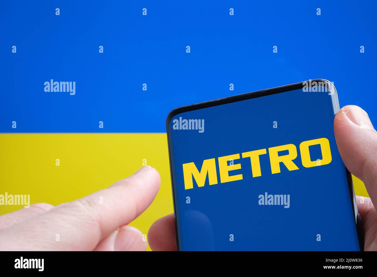 METRO Cash e Carry Company logo sullo smartphone e bandiera Ucraina sullo sfondo. Concetto. Stafford, Regno Unito, 20 marzo 2022 Foto Stock