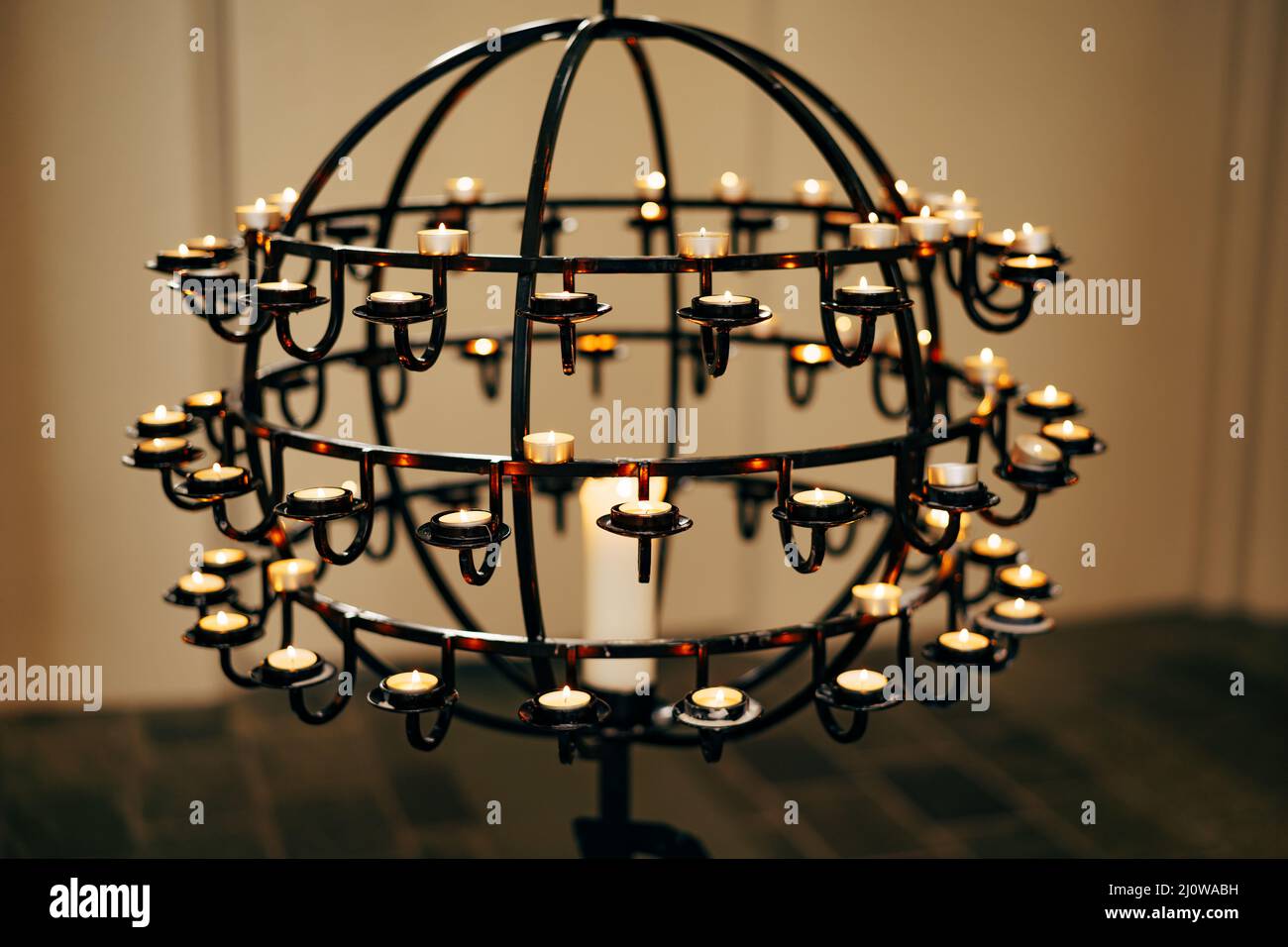 Candele votive si trovano su un piedistallo a forma di palla in una chiesa Foto Stock