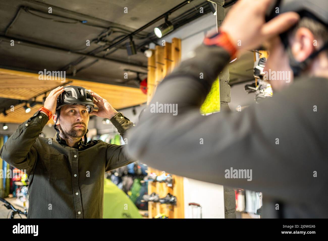 Il giovane uomo è venuto al negozio di biciclette. Sta misurando il casco. Il maschio sceglie il casco nel negozio di attrezzature sportive. Acquisto di nuovo Foto Stock