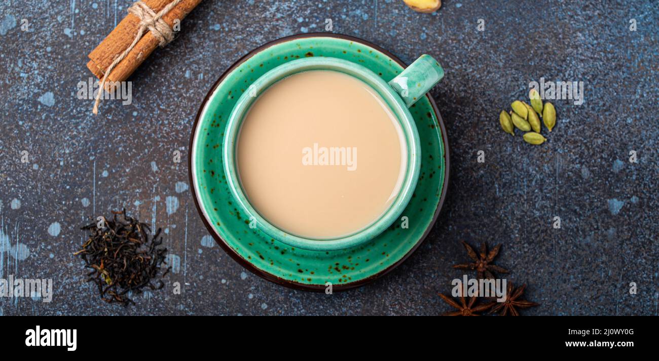 Tè indiano bevanda calda con latte e spezie in rustico verde teacup con ingredienti per la preparazione di masala chai Foto Stock