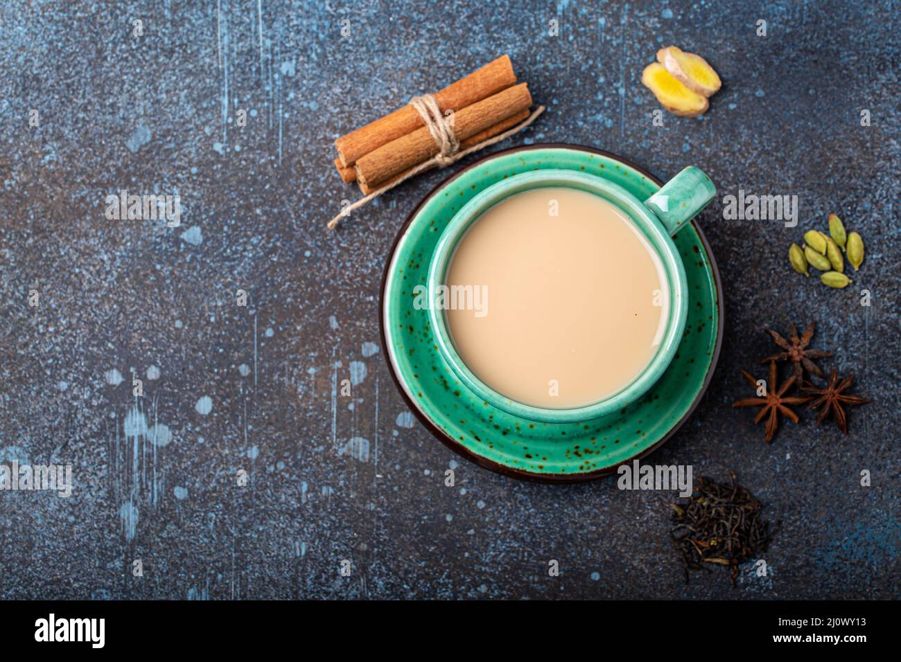 Tè indiano bevanda calda con latte e spezie in rustico verde teacup con ingredienti per la preparazione di masala chai Foto Stock