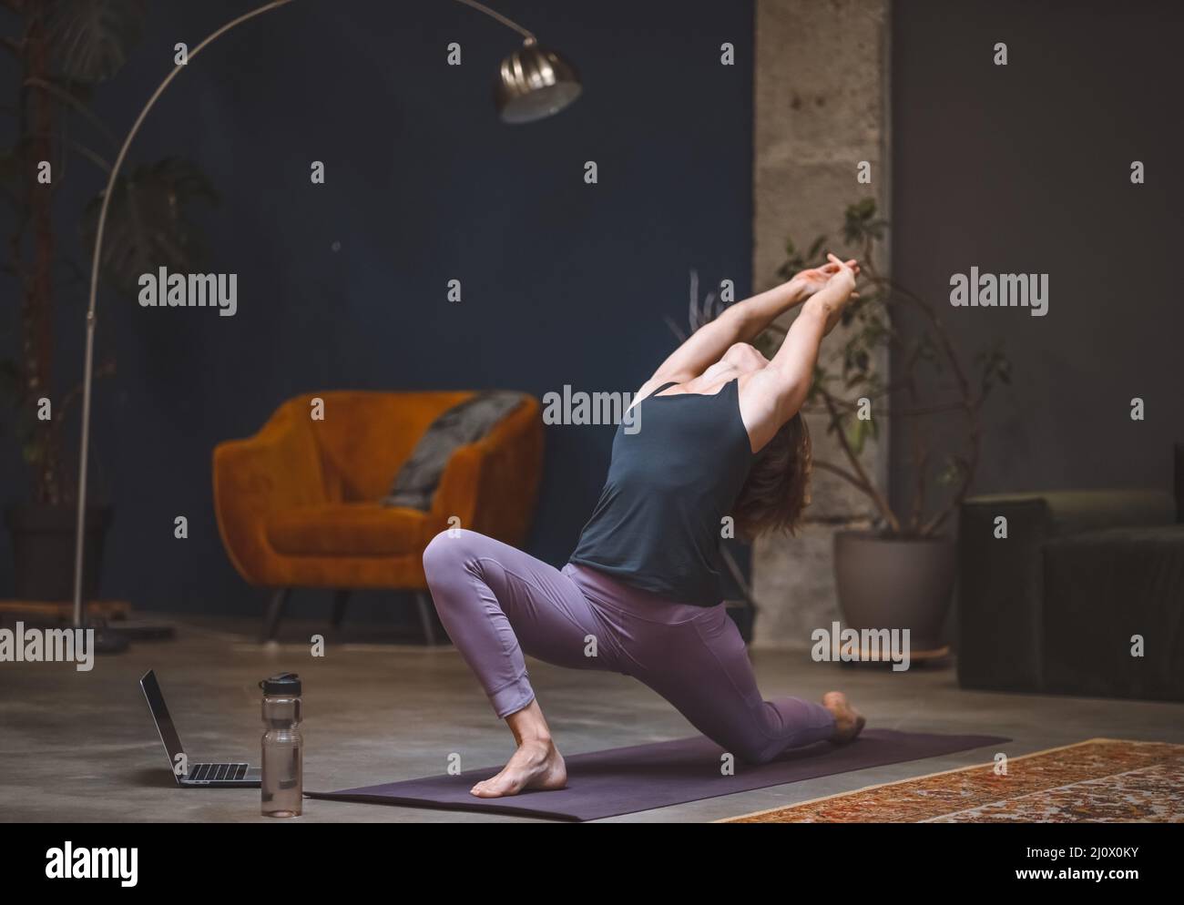 La giovane donna esegue lo yoga stretching facendo Anjaneyasana o bassa affondo posa in moderna casa interna. Donna che pratica yoga a casa. Foto Stock