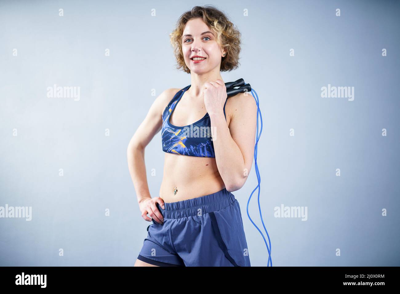 Uno sportivo sorridente in posa con una corda che salta. Femmina con corpo muscolare in posa con corda di salto. Modello fitness. Positività del corpo Foto Stock