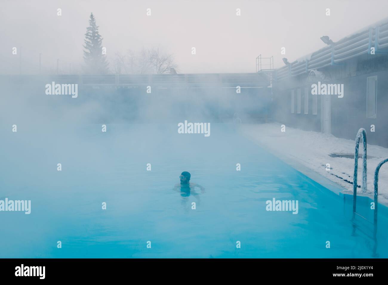 Fit nuotatore maschile allenamento nuoto in piscina invernale aperta con nebbia. Concetto di spa geotermica all'aperto. Foto Stock