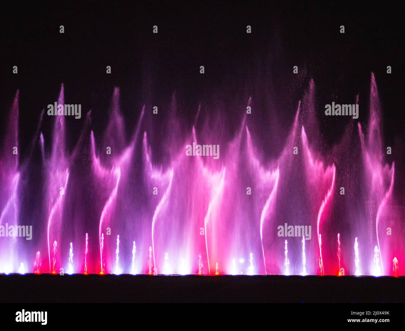 Bella fontana danzante spettacolo con riflessione sull'acqua di notte. Foto Stock