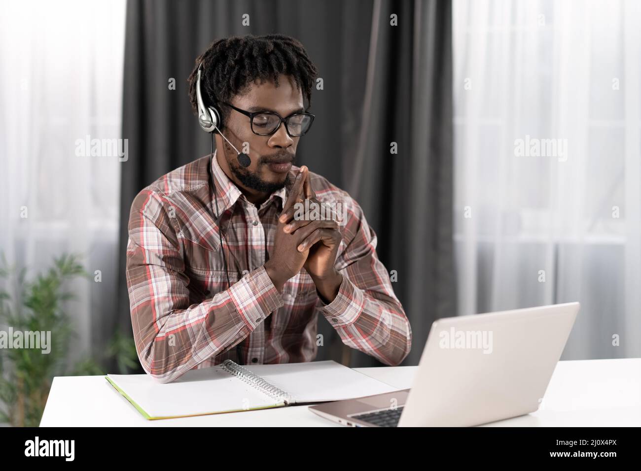 Freelance afroamericani che guardano un notebook con cuffie che hanno una videochiamata di gruppo che lavora lontano a casa. Giovane studente Foto Stock