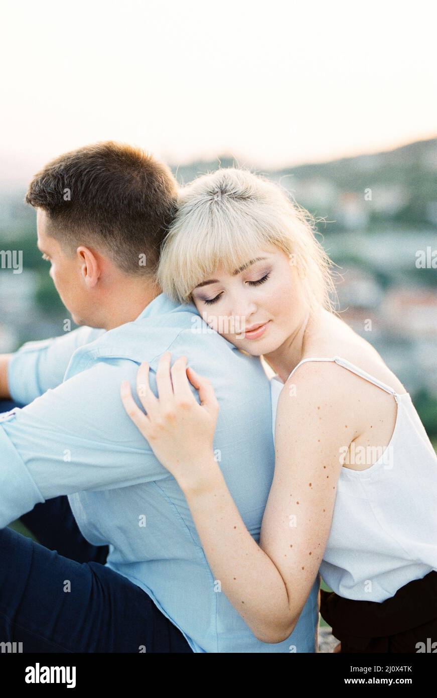 La donna abbraccia un uomo da dietro con la testa sulla spalla. Verticale Foto Stock