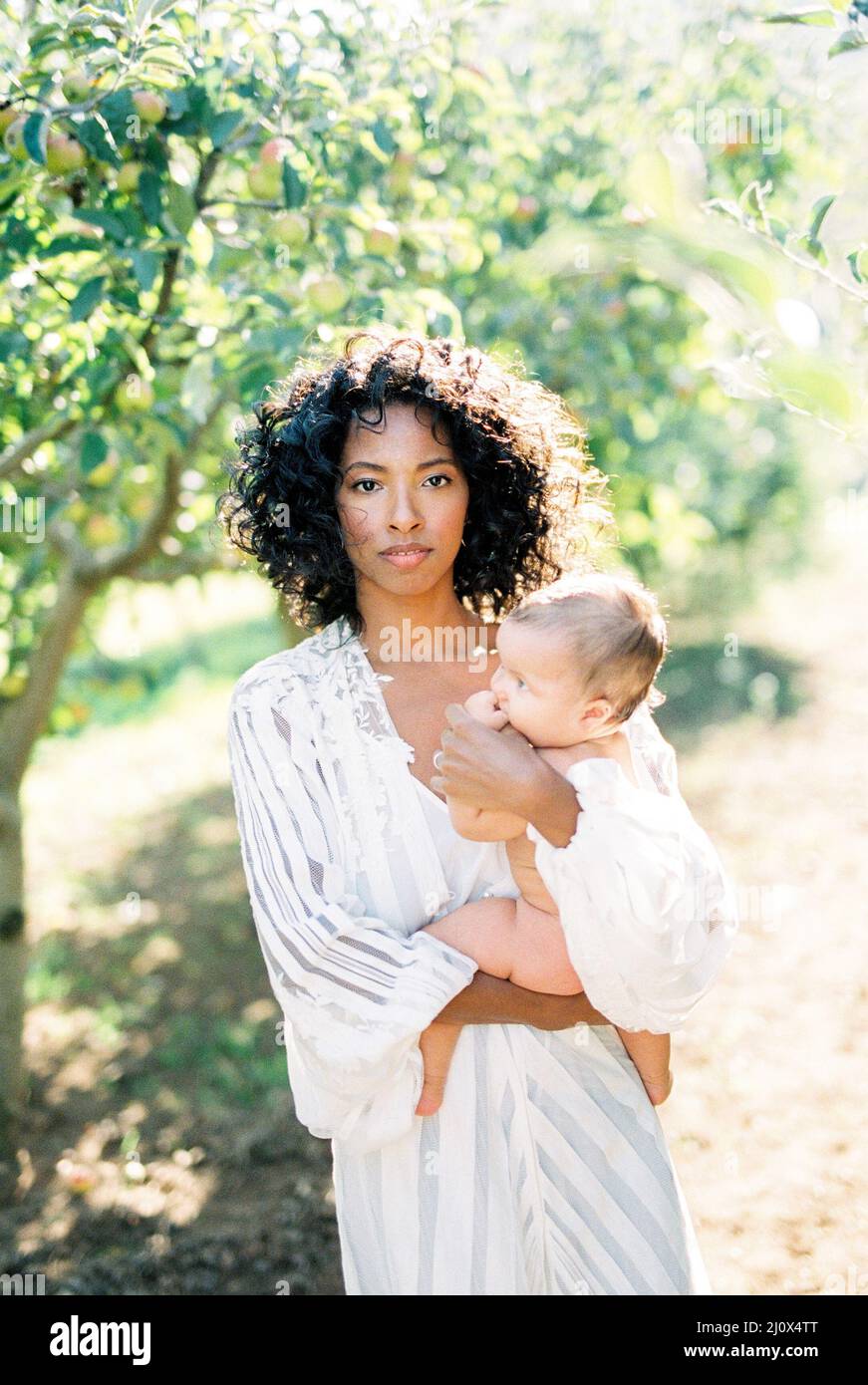 Donna con un neonato in braccio si erge in giardino Foto Stock