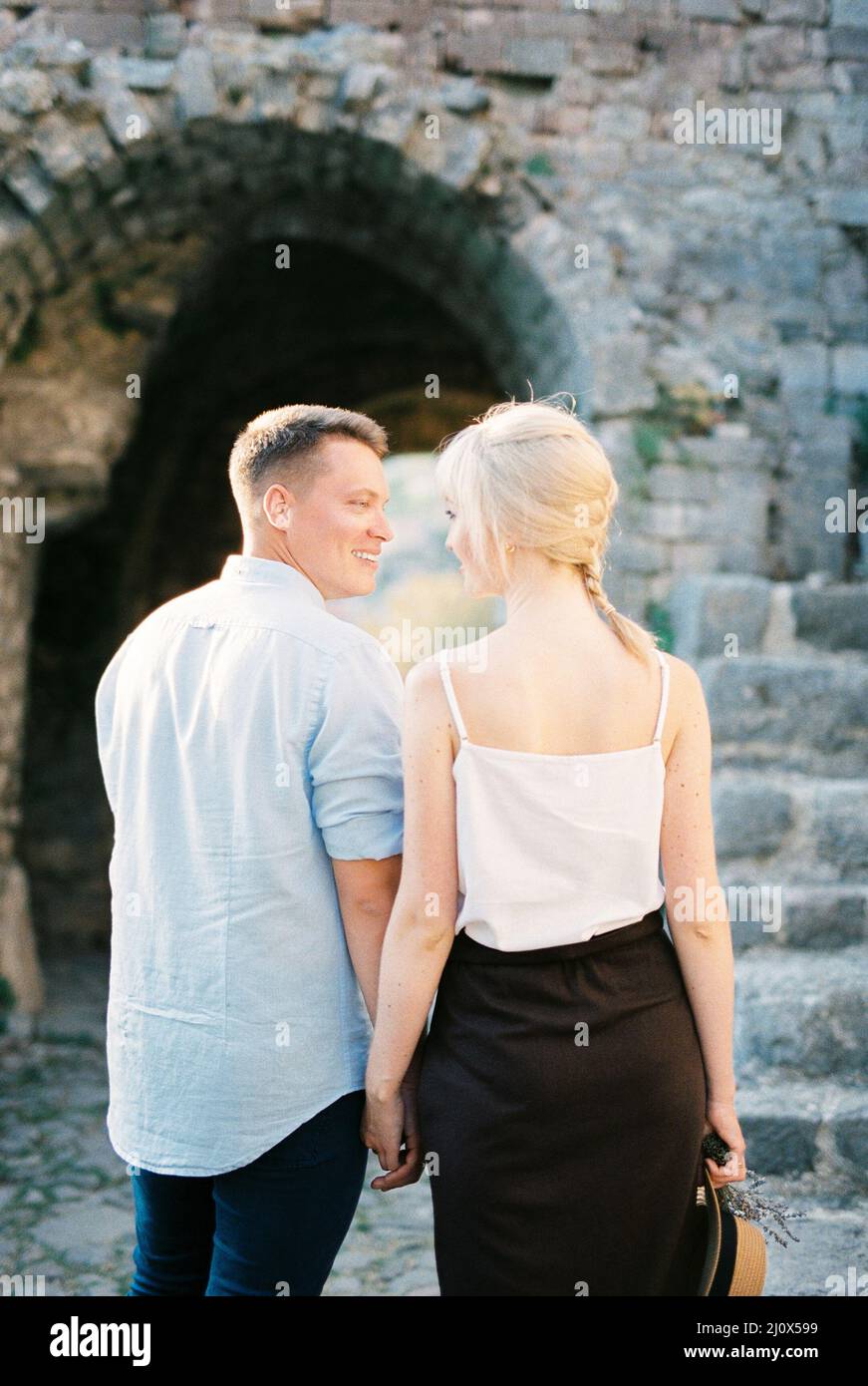 L'uomo e la donna tengono le mani vicino ad un arco di pietra. Vista posteriore Foto Stock
