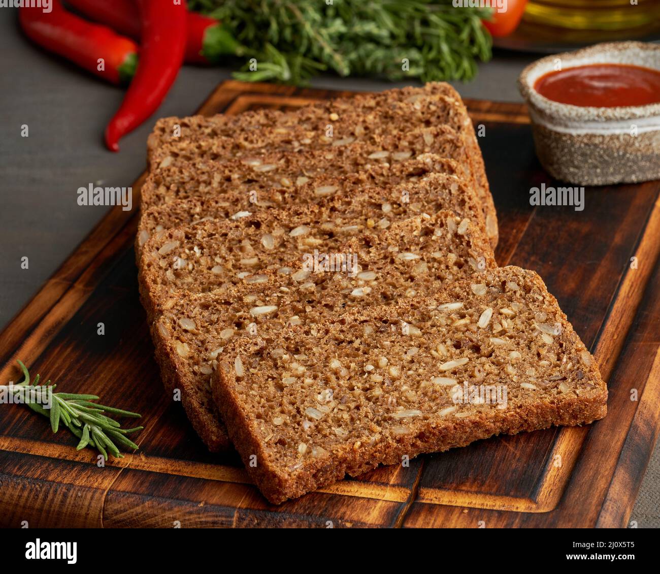 Tostare il pane di grano di segale su un tagliere di legno su sfondo marrone scuro. Foto Stock