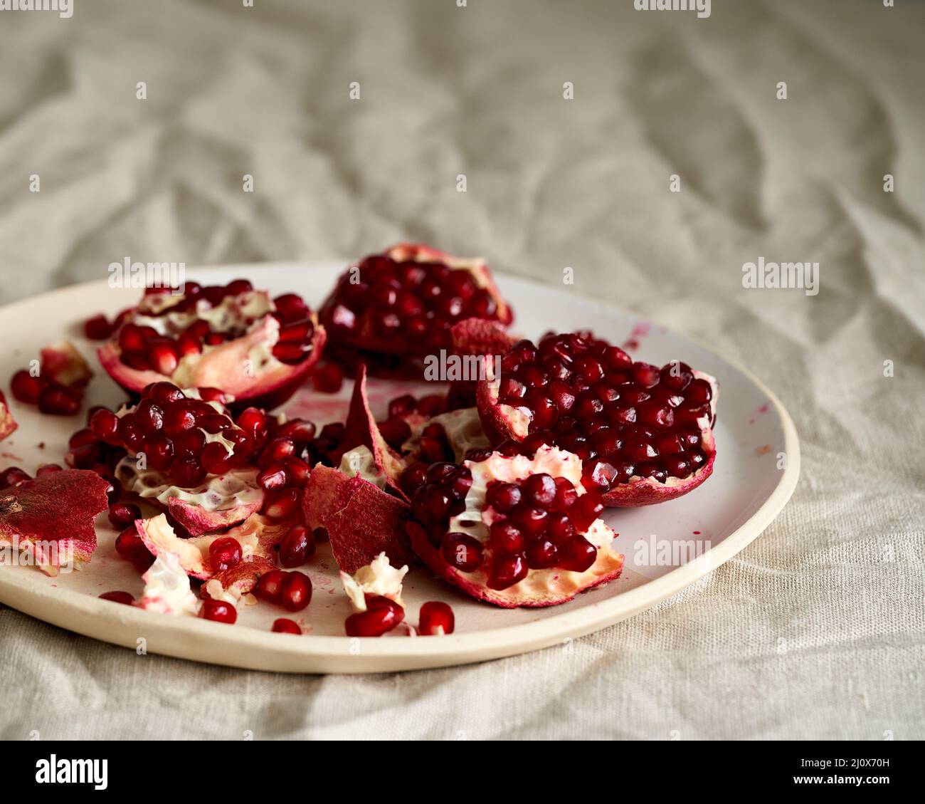 Ancora vita con melograno aperto rotto e semi su piastra su tavolo coperto con tovaglia beige sbriciolato Foto Stock