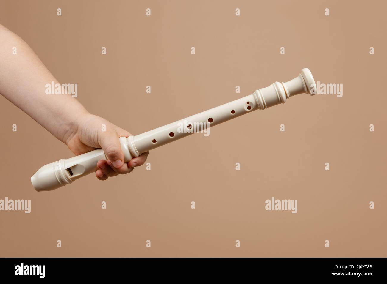 Tenere il flauto di colore avorio comune con una mano closeup, sfondo beige. Strumento musicale Woodwind. Foto Stock