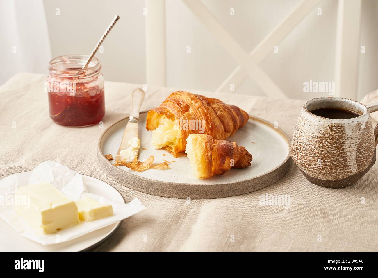 Deliziosi croissant sul piatto e bevanda calda in tazza, marmellata e burro. Foto Stock