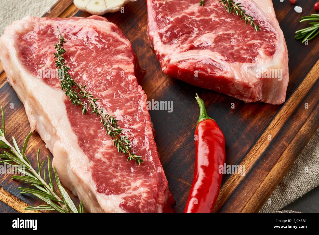 Due grandi pezzi interi di carne di manzo cruda, striploin su tagliere di legno, macro, primo piano Foto Stock