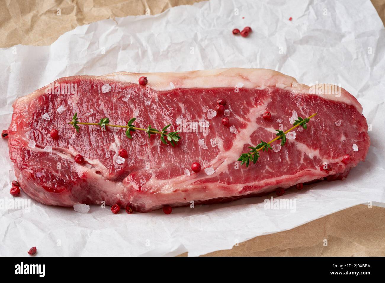Grande pezzo intero di carne di manzo cruda, striploin su carta pergamena bianca Foto Stock