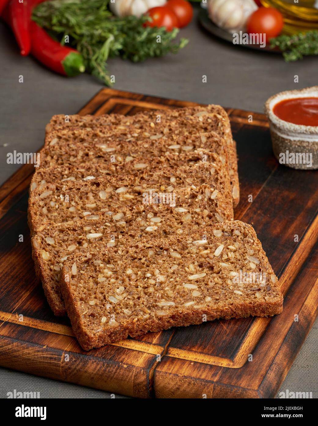 Tostare il pane di grano di segale su un tagliere di legno su sfondo marrone scuro. Foto Stock