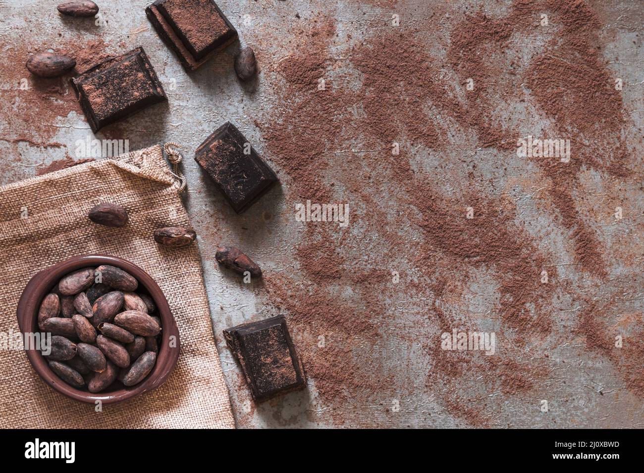 Polvere di cacao sparsa con ciotola di cacao in pezzi di cioccolato Foto Stock