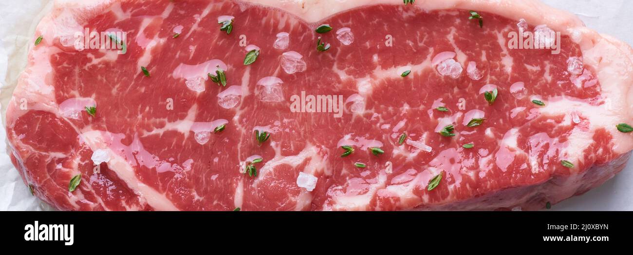 Striscione a larghezza lunga con grosso pezzo intero di carne di manzo cruda, striploin. Bistecca con condimento e sale. Foto Stock