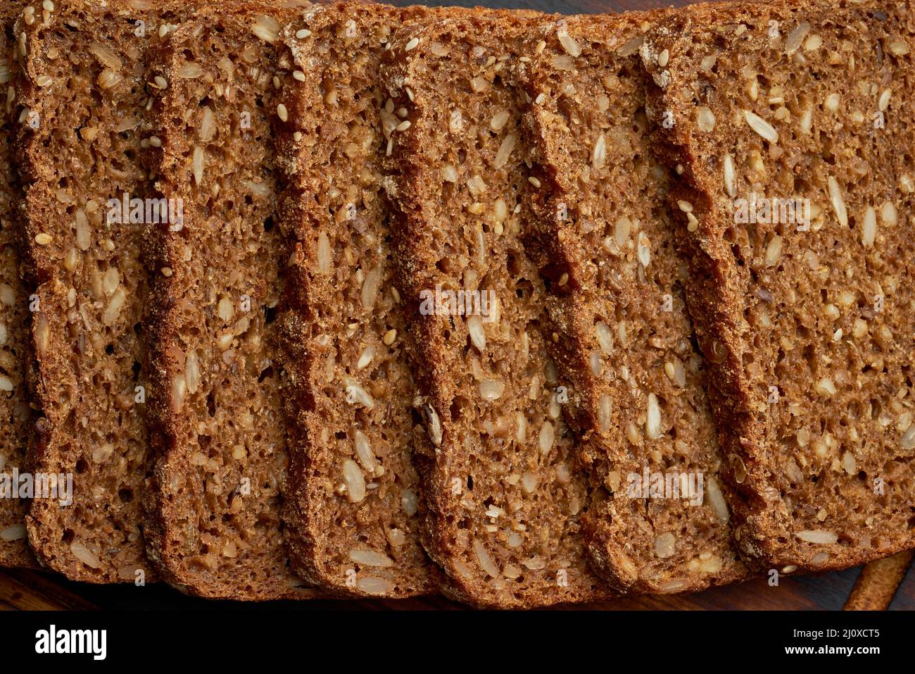 Tostare il pane di grano di segale su un tagliere di legno su sfondo marrone scuro. Foto Stock