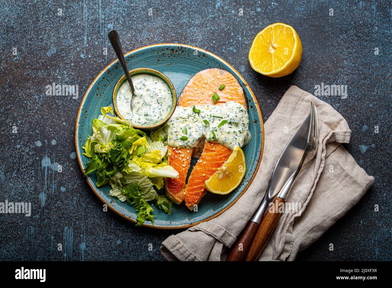 Pasto sano cotto bistecche di salmone alla griglia con salsa di aneto e foglie di insalata sul piatto Foto Stock