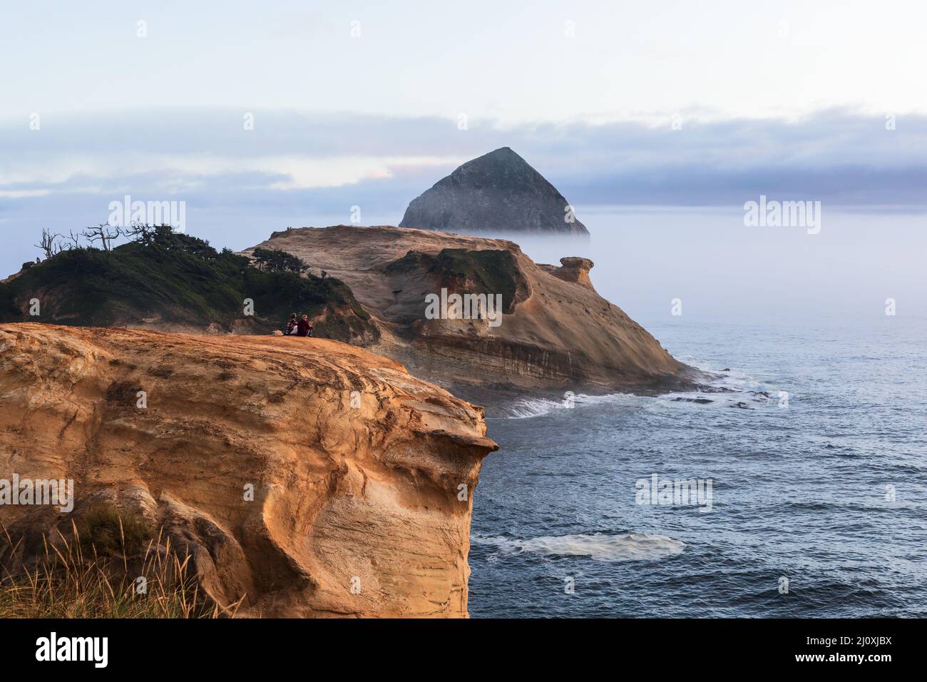 Una coppia guarda il tramonto sulla costa dell'Oregon a Cape Kiwanda a Pacific City Foto Stock