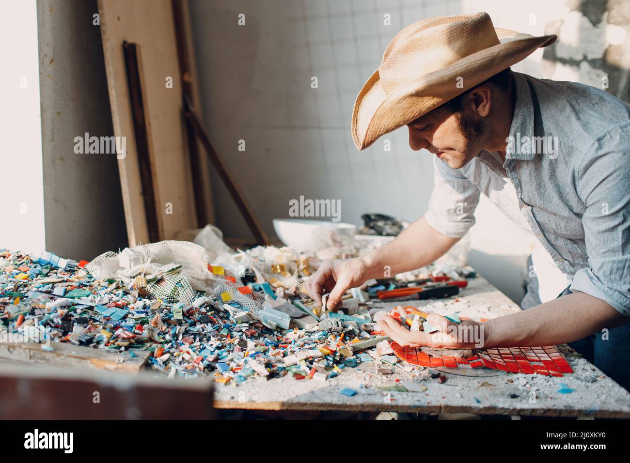 Uomo Mosaics master sceglie pezzi di vetro smalti selezionati per pannello mosaico. Mosaicista maschile al lavoro. Foto Stock