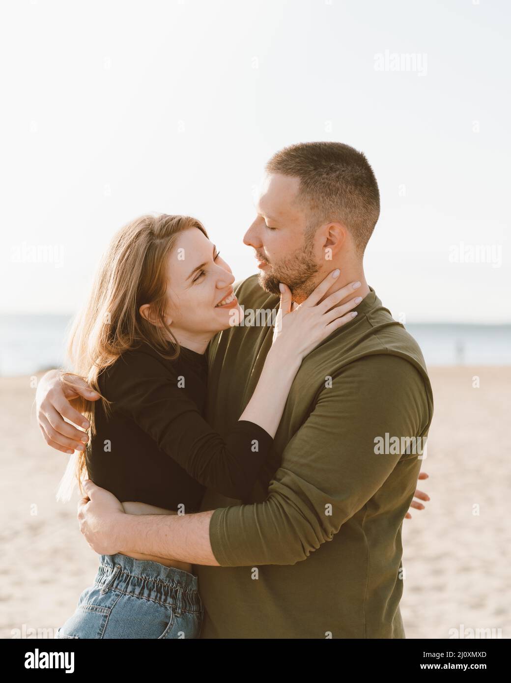 Giovane coppia adulta in piedi sulla spiaggia, guardandosi l'un l'altro. Uomo che abbraccia donna ridente Foto Stock