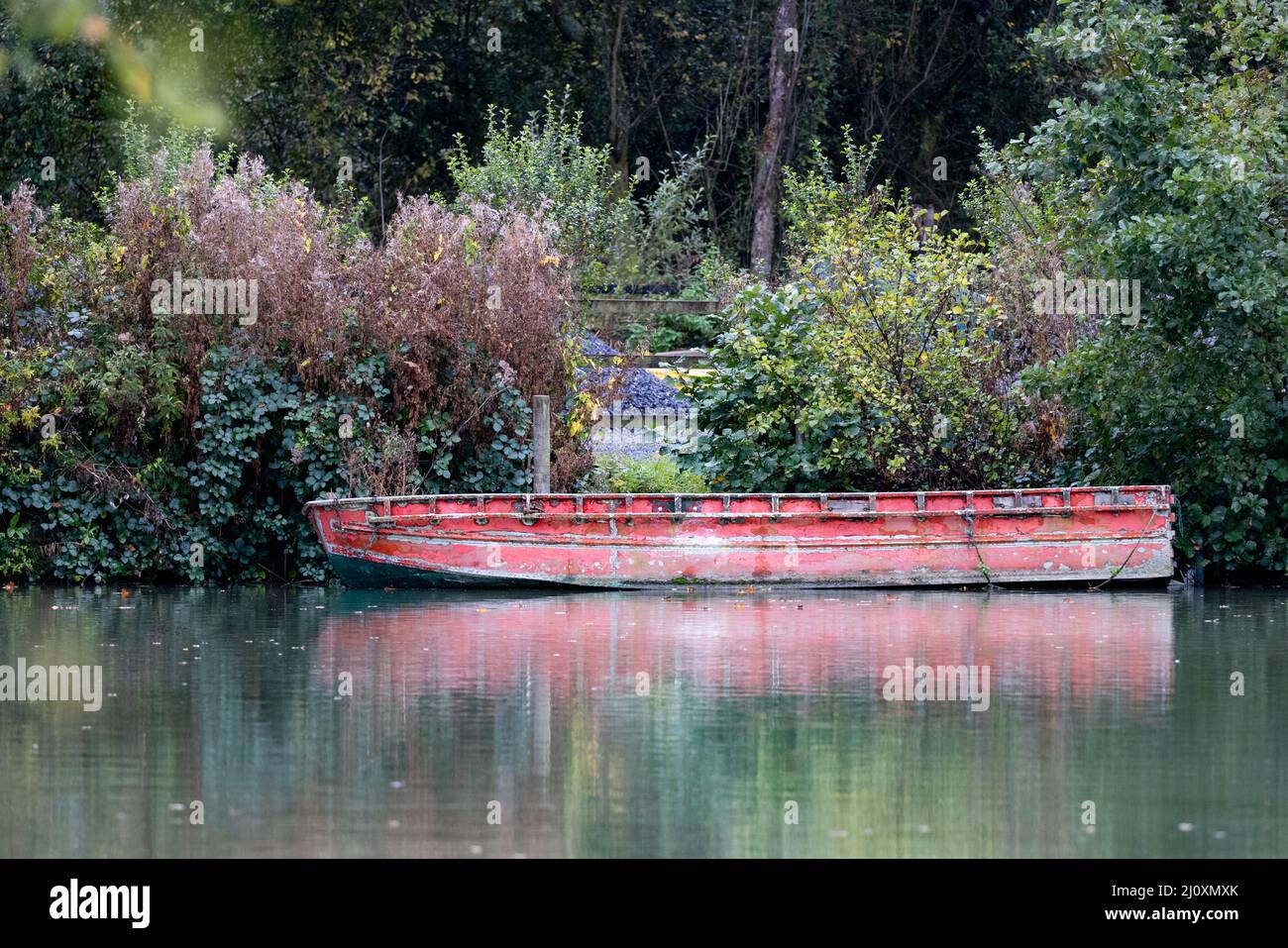 Vecchia barca con vernice rossa sbiadita sul lago di pesca con riflessione, Somerset, Regno Unito Foto Stock