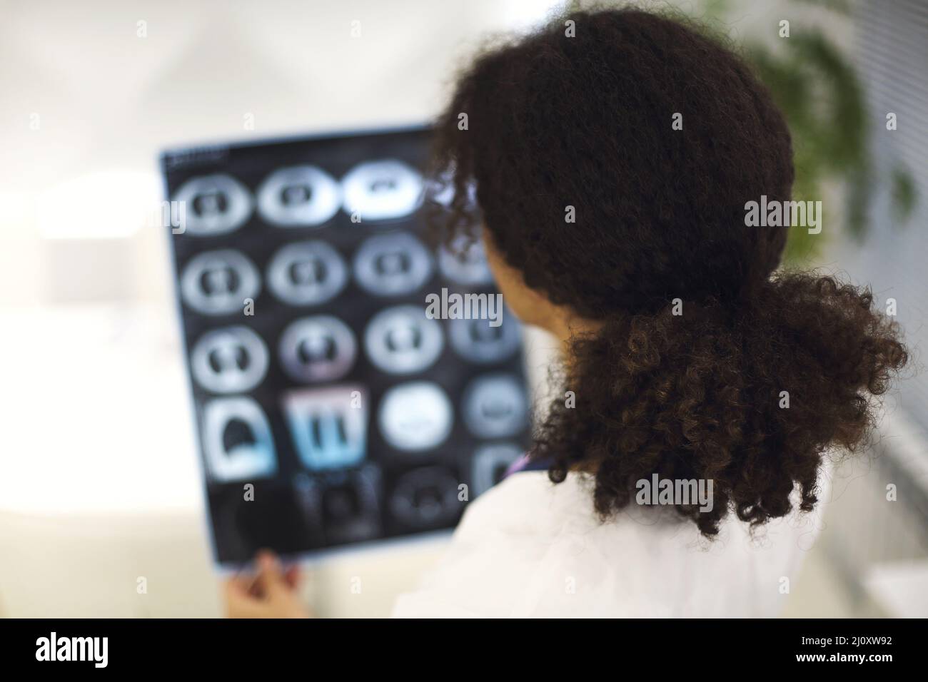 Vista posteriore di un medico di etnia femminile che analizza raggi X, scansione MRI o screening TC durante il lavoro in ospedale Foto Stock
