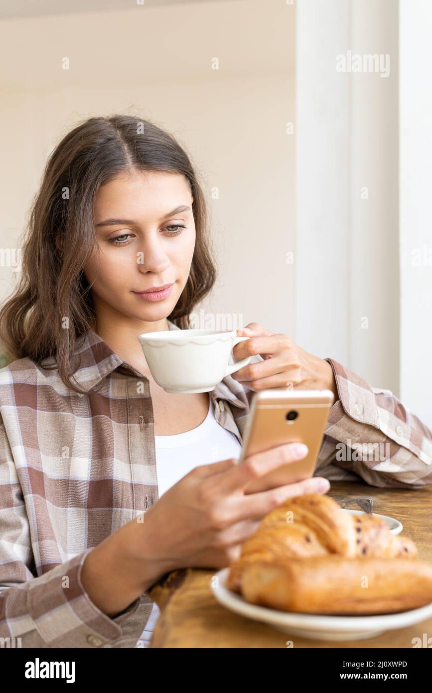 Donna in cerca di informazioni su Internet, utilizzando il cellulare, durante la colazione. Concetto Foto Stock