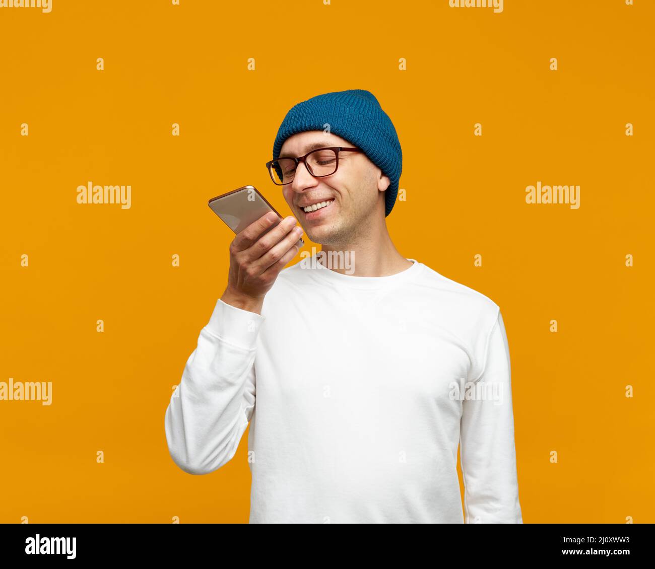 Ritratto del giovane positivo che registra il messaggio audio, parlando al microfono del telefono cellulare Foto Stock