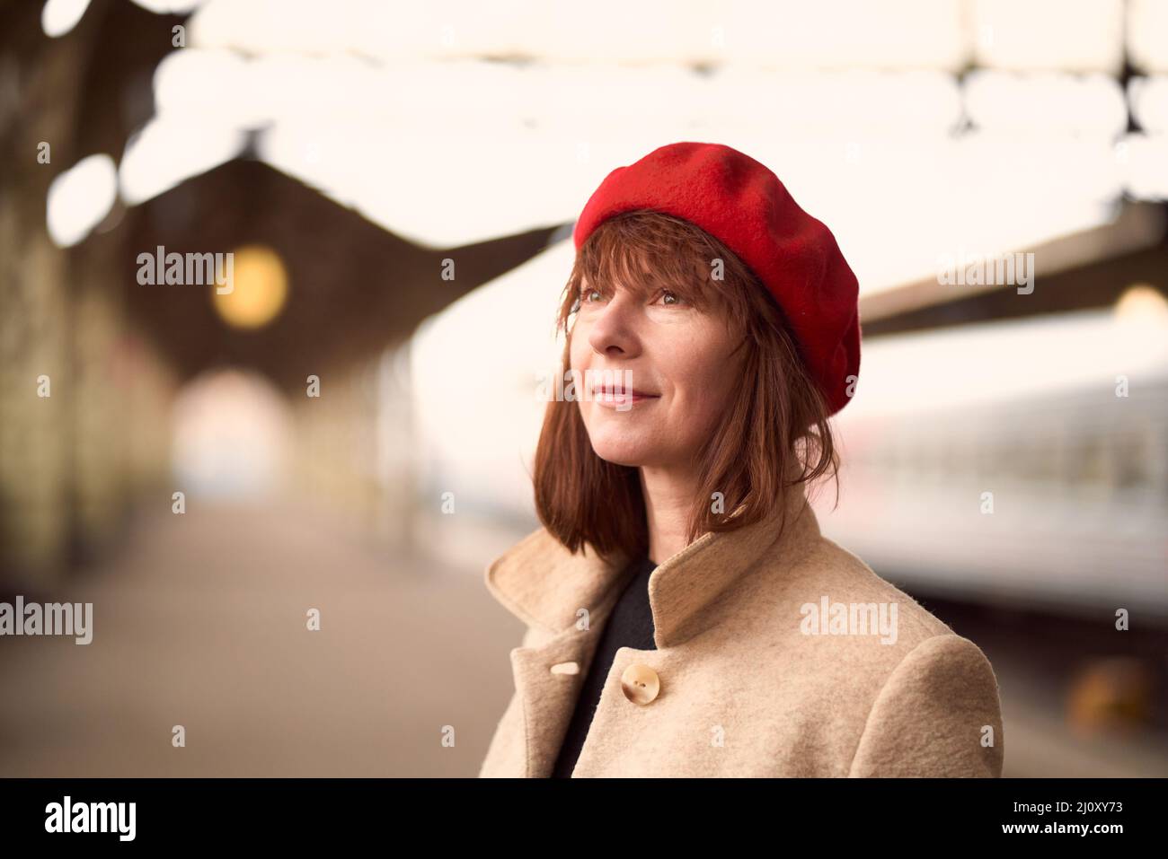Primo piano ritratto di bella donna, sorridente e in attesa di treno sulla stazione ferroviaria. La ragazza viaggia leggero Foto Stock