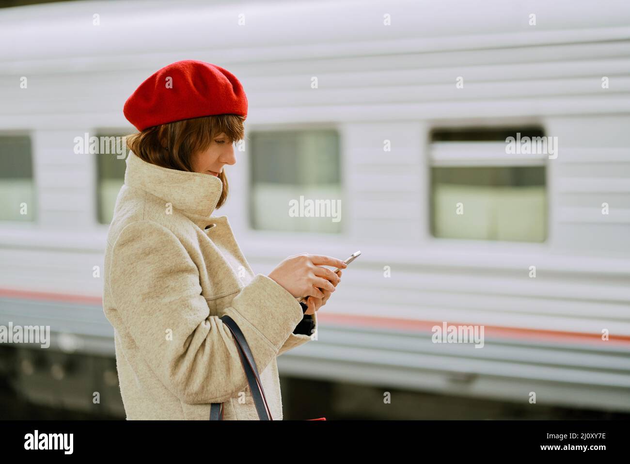 Stazione ferroviaria. Bella ragazza è in attesa di treno e guarda il telefono cellulare. La donna viaggia leggero. Foto Stock