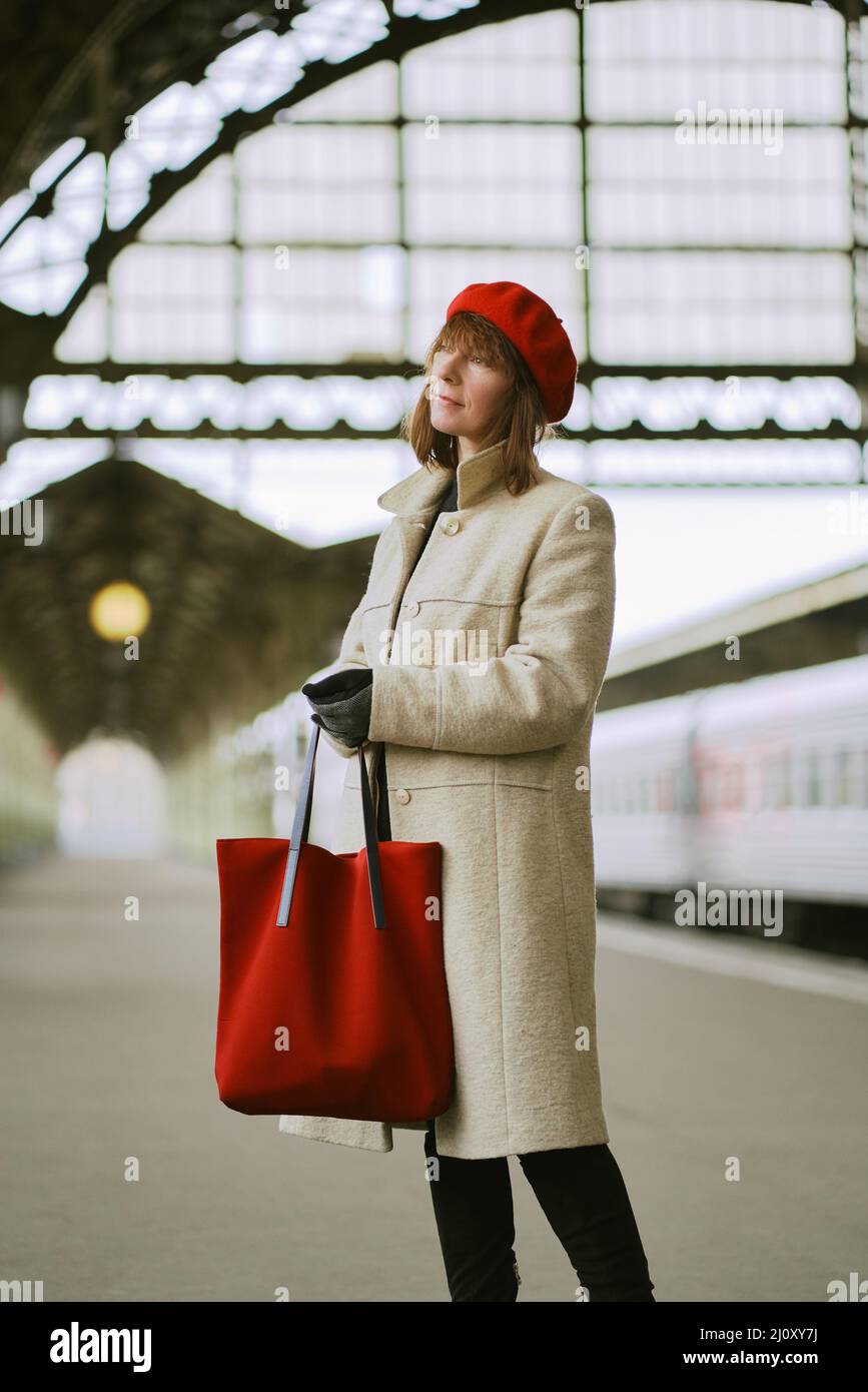Bella donna sta aspettando il treno sulla stazione ferroviaria. La ragazza viaggia leggero. Femmina di mezza età Foto Stock