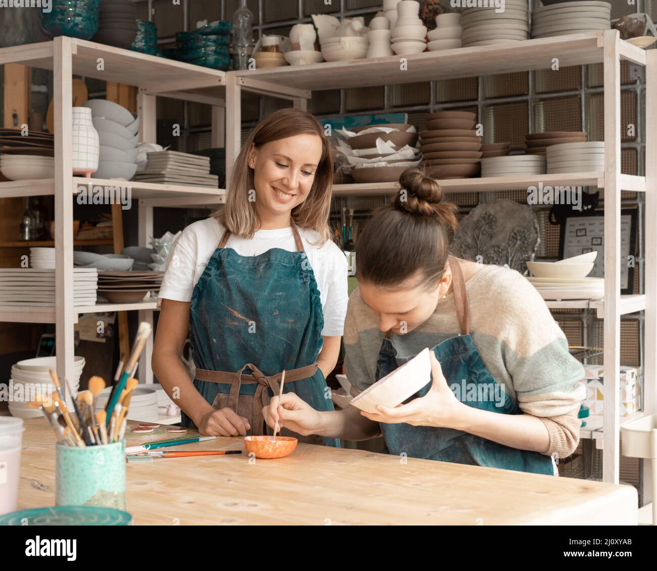 Donna che fa ceramica. Attraente giovane donna esperta in grembiule in piedi al tavolo e l'insegnamento Foto Stock