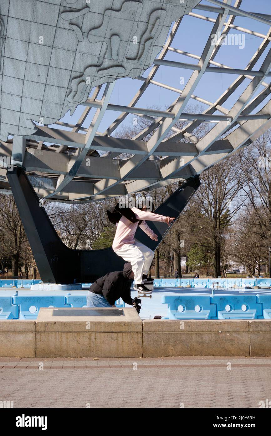 All'ombra dell'Unisphere, uno skater stunt salta su un ostacolo mentre un altro skater lo filma. In un parco a Queens, New York City. Foto Stock
