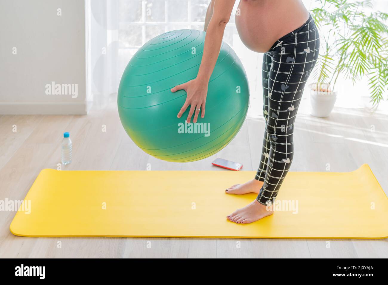 la giovane donna incinta fa sport per rimanere attiva in gravidanza sollevando una palla fitness nel suo soggiorno. assistenza sanitaria, allenamento e sport a casa Foto Stock