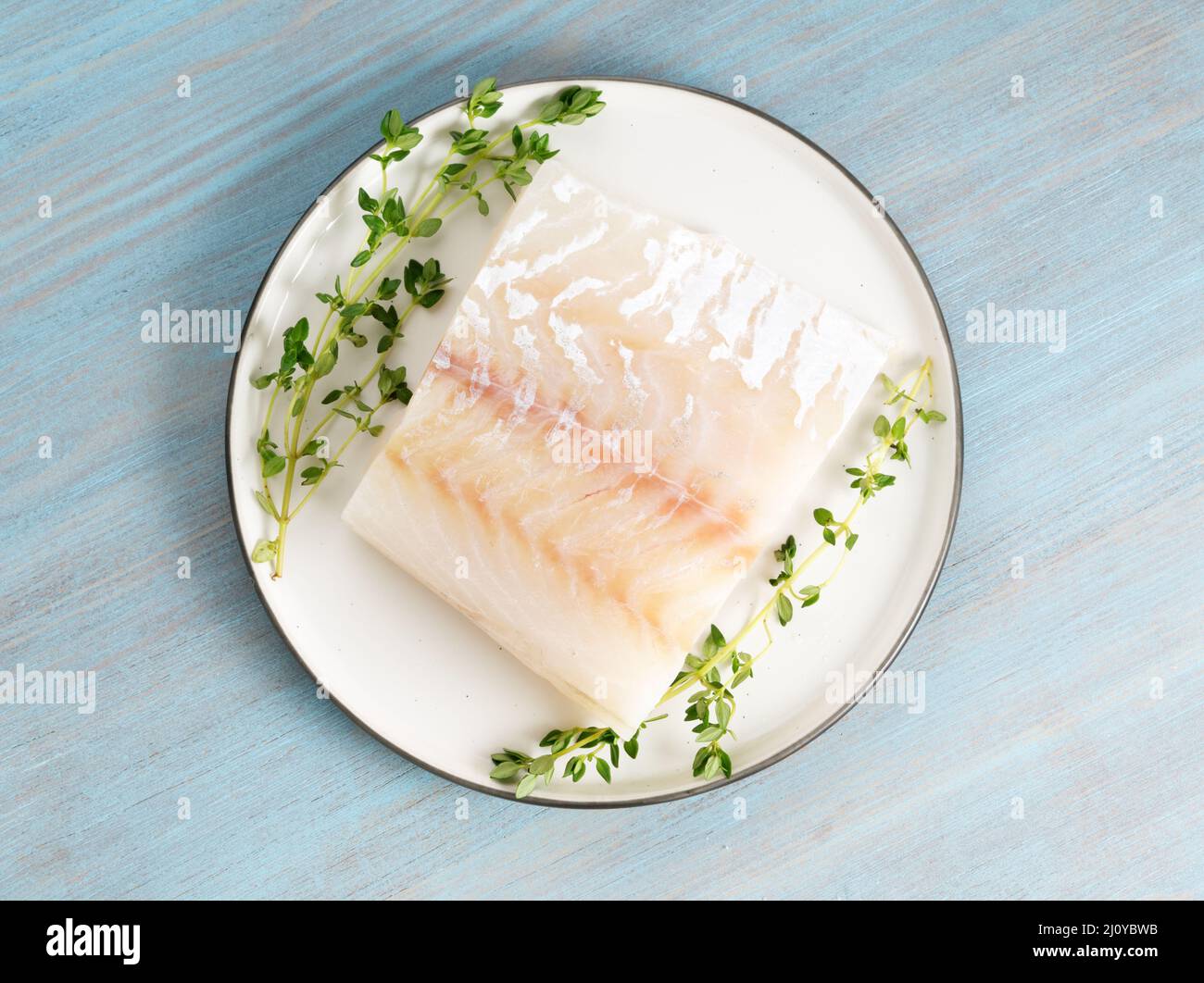 Pezzo di filetto di merluzzo crudo sul piatto su tavola di legno blu, vista dall'alto Foto Stock