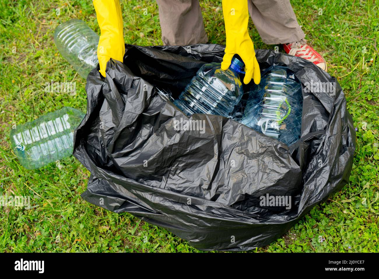 Separare la procedura di garbage collection. Mani in Guanti gialli mettendo grandi bottiglie di plastica in bllack immondizia di plastica in borsa. Foto Stock