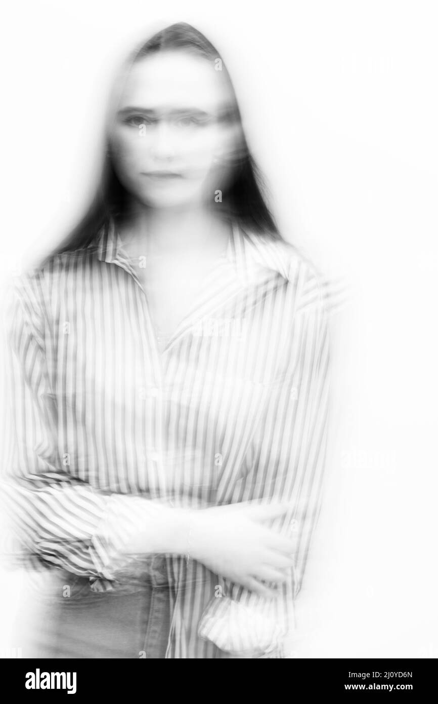 Ritratto astratto in bianco e nero con capelli lunghi e scuri in movimento sfocati e sfondo bianco. Modello con jeans e bluse a righe. Co. Immagine Foto Stock