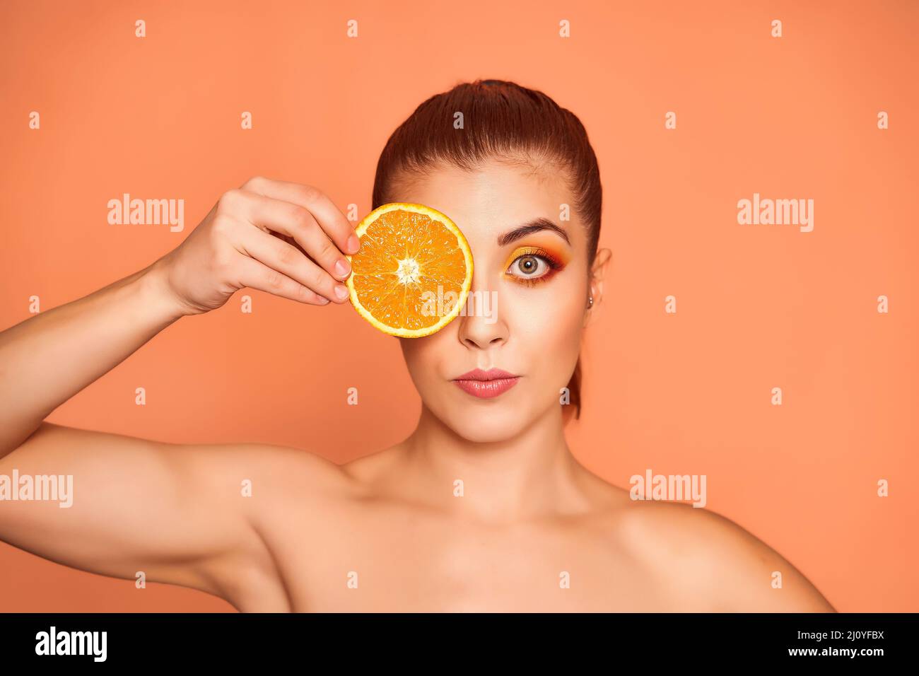 Ritratto closeup di bella ragazza felice tenendo metà delle arance vicino faccia, isolato su sfondo arancione. Concetto di bellezza e assistenza sanitaria. Foto di alta qualità Foto Stock