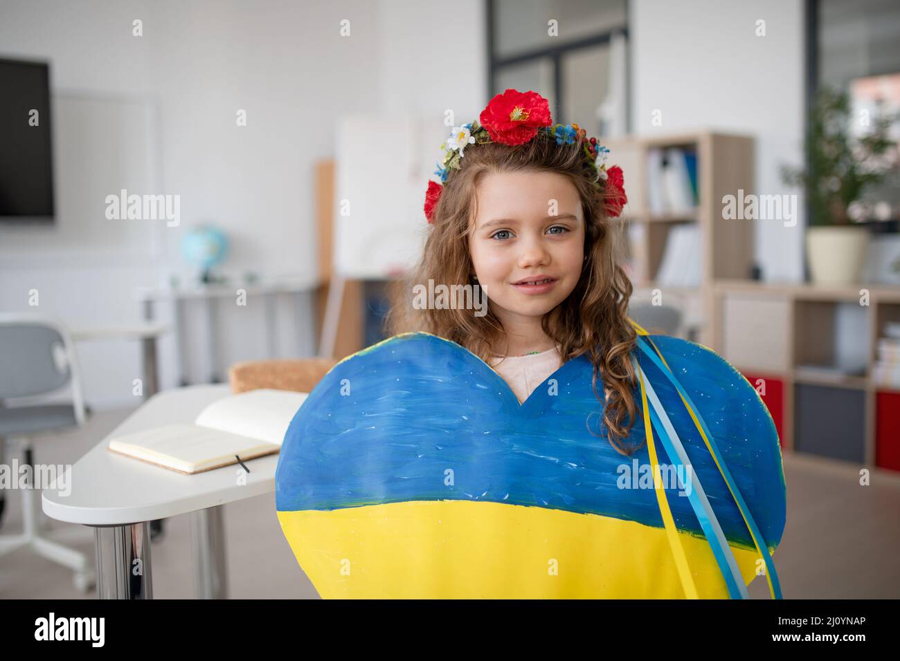 Piccola studentessa Ucraina che tiene il cuore in colori ucraini e guarda la macchina fotografica a scuola. Foto Stock