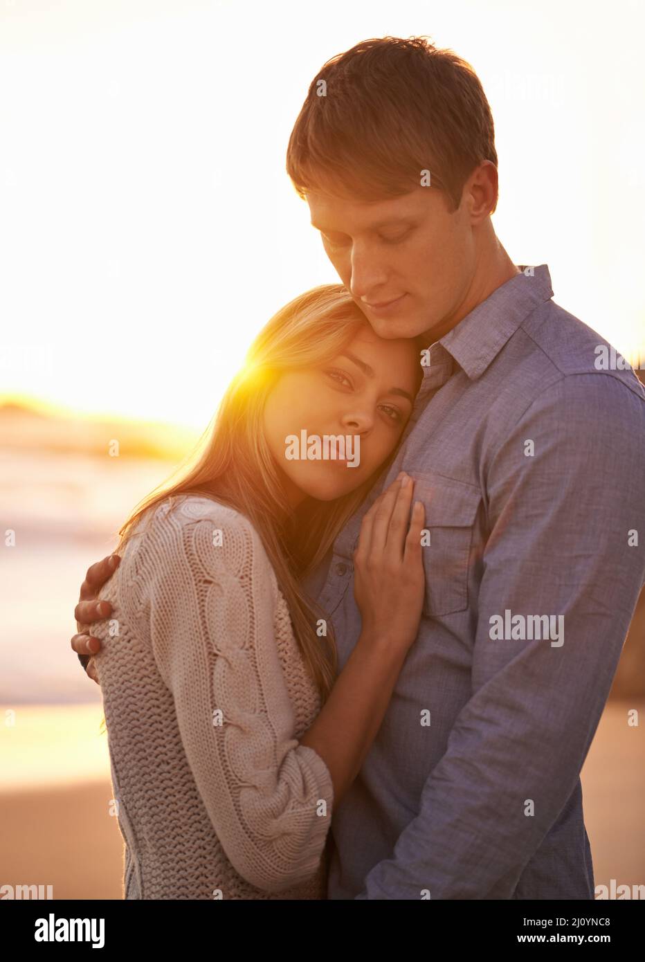 Un momento fra le mie braccia ma per sempre nel mio cuore. Ritratto di una giovane coppia felice godendo di un romantico abbraccio sulla spiaggia al tramonto. Foto Stock